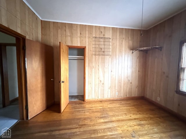 unfurnished bedroom featuring wooden walls, baseboards, and wood finished floors
