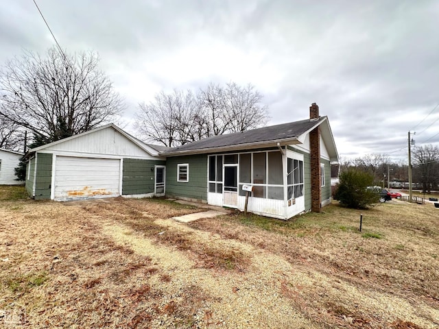 rear view of house with roof with shingles, a sunroom, driveway, and a chimney