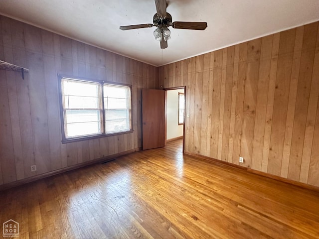 unfurnished room featuring wooden walls, baseboards, ceiling fan, and hardwood / wood-style flooring