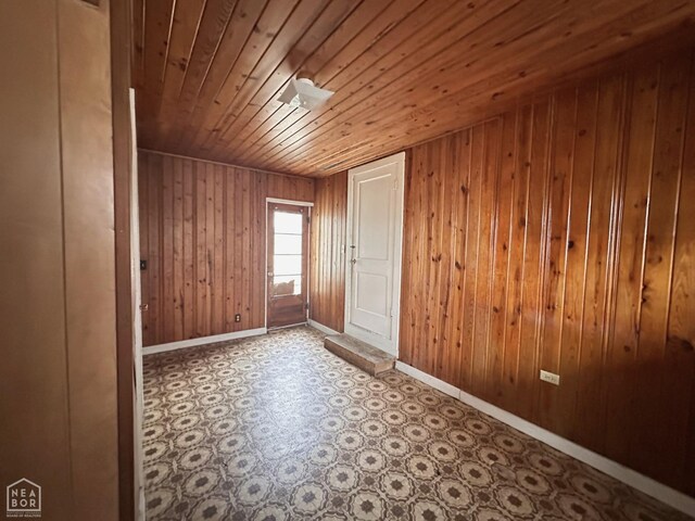 unfurnished room featuring wood ceiling, wooden walls, baseboards, and tile patterned floors