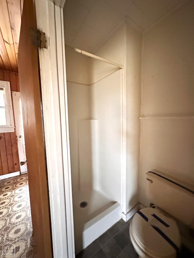 bathroom featuring wood walls, toilet, and a stall shower
