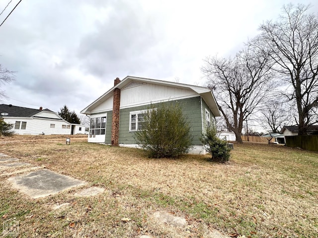 view of side of property featuring a chimney, fence, and a yard