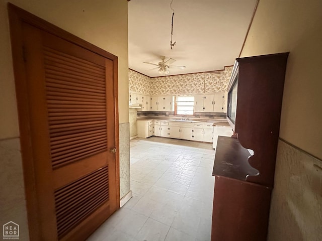 kitchen featuring white cabinets, a sink, a ceiling fan, wallpapered walls, and light floors