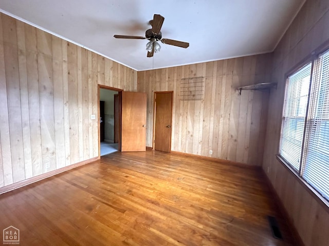 spare room featuring wood walls, baseboards, a ceiling fan, and wood finished floors
