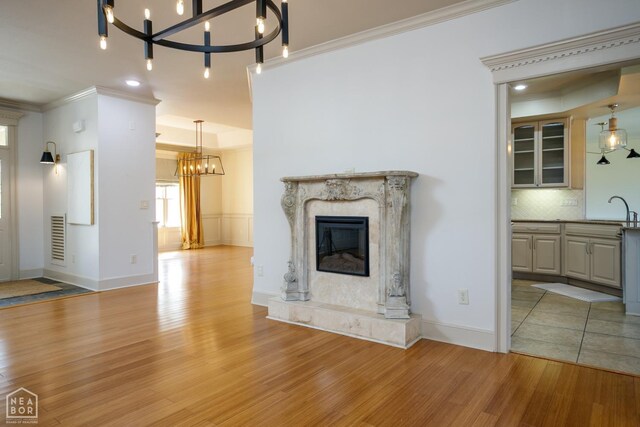 unfurnished living room featuring a fireplace, light wood-type flooring, ornamental molding, a chandelier, and a sink