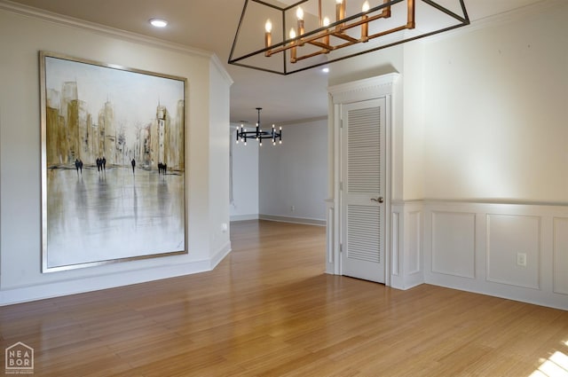interior space featuring a decorative wall, an inviting chandelier, ornamental molding, and wood finished floors