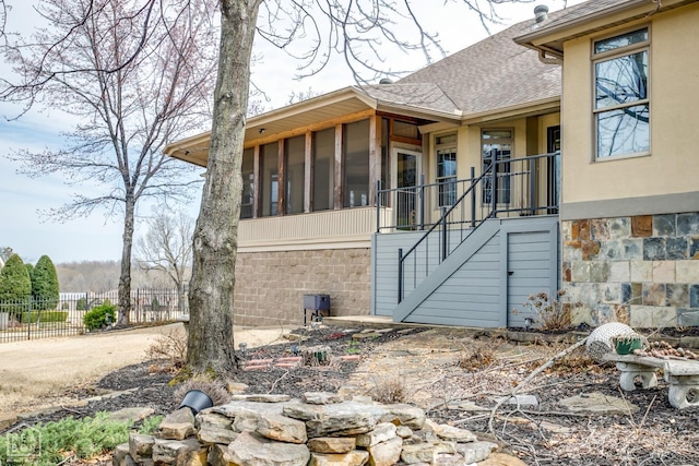 view of side of property with stucco siding, stairway, a sunroom, fence, and a shingled roof