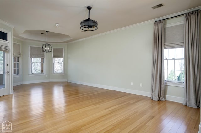 spare room with ornamental molding, a chandelier, visible vents, a tray ceiling, and light wood finished floors