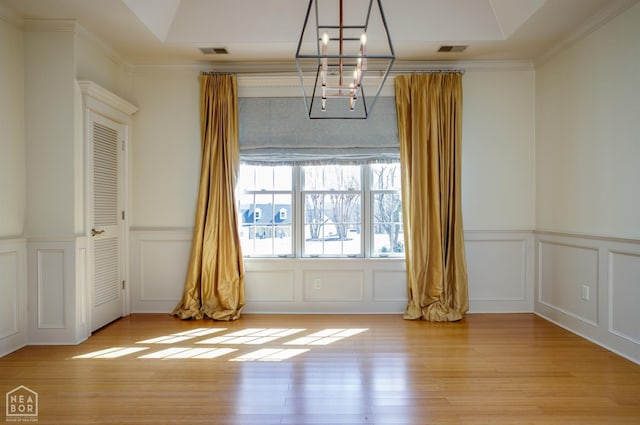 unfurnished dining area with a decorative wall, visible vents, an inviting chandelier, and light wood-style floors