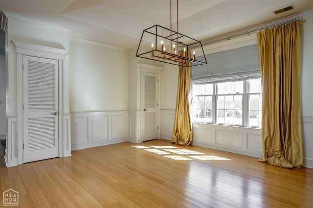 unfurnished dining area featuring a decorative wall, visible vents, light wood-style flooring, and an inviting chandelier