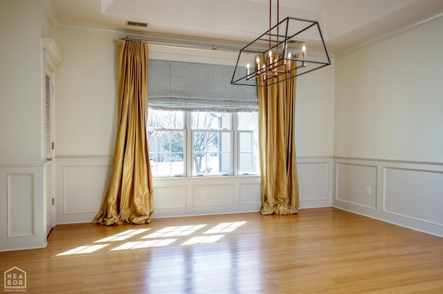unfurnished dining area featuring a decorative wall, a notable chandelier, light wood-type flooring, and crown molding