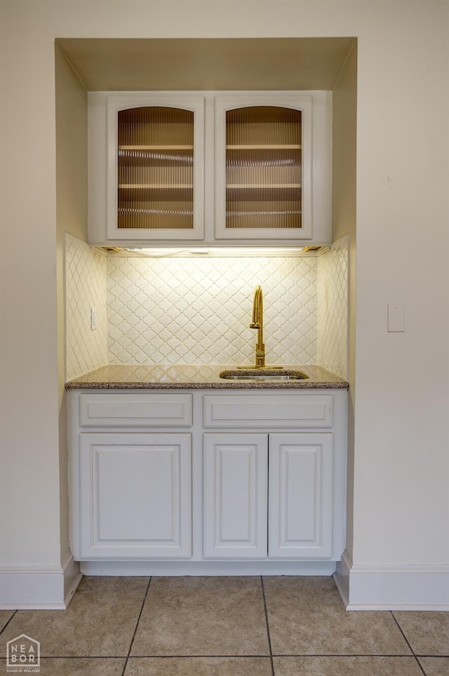 bar with light tile patterned floors, baseboards, indoor wet bar, a sink, and backsplash