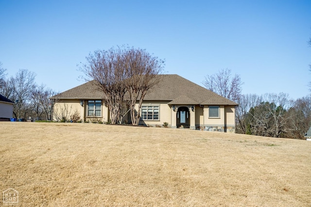 ranch-style home featuring roof with shingles, stucco siding, and a front lawn