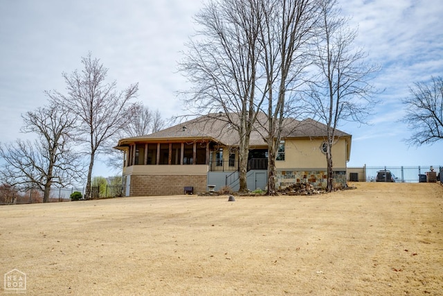 back of house with fence, stone siding, a sunroom, and stucco siding
