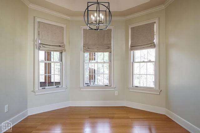 empty room with a chandelier, wood finished floors, baseboards, and ornamental molding
