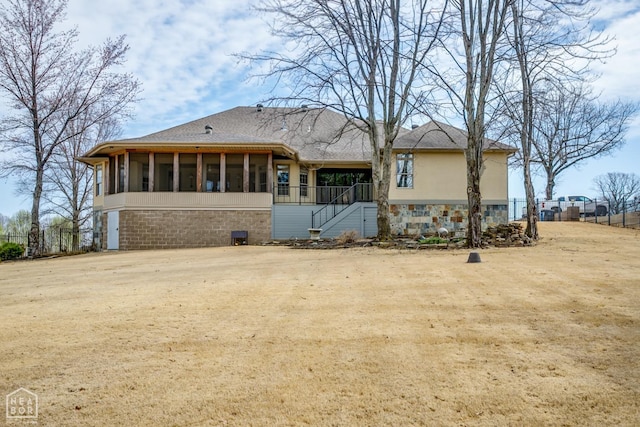 back of property featuring stone siding, a sunroom, and roof with shingles