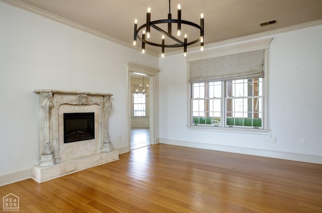 unfurnished living room featuring a notable chandelier, ornamental molding, visible vents, wood finished floors, and a premium fireplace