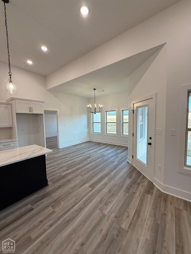 unfurnished living room featuring baseboards, recessed lighting, a notable chandelier, and wood finished floors
