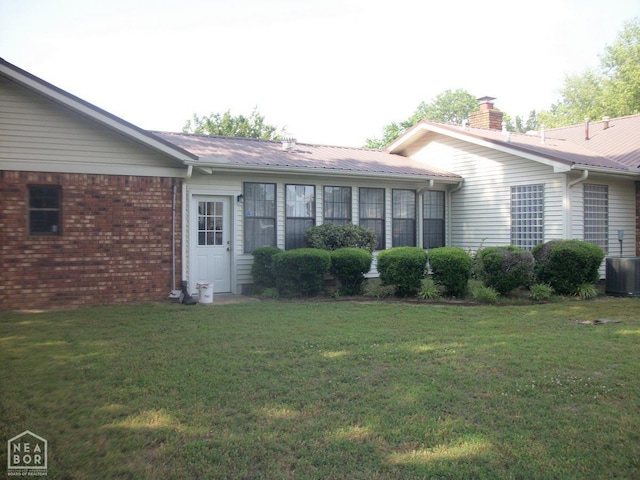 exterior space featuring central air condition unit, a chimney, brick siding, and a lawn