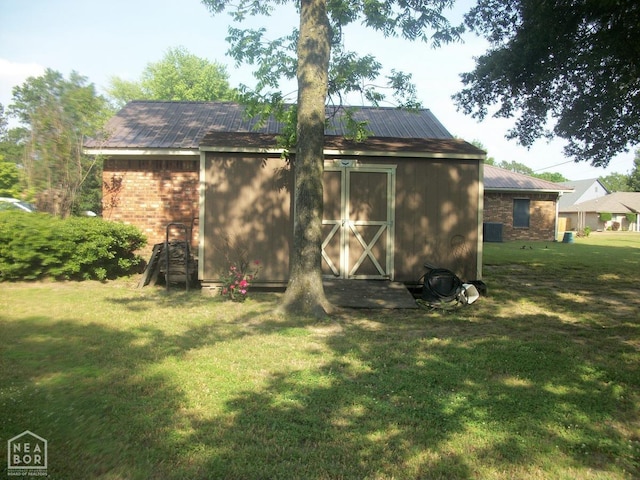 back of house with an outbuilding, brick siding, a lawn, and metal roof