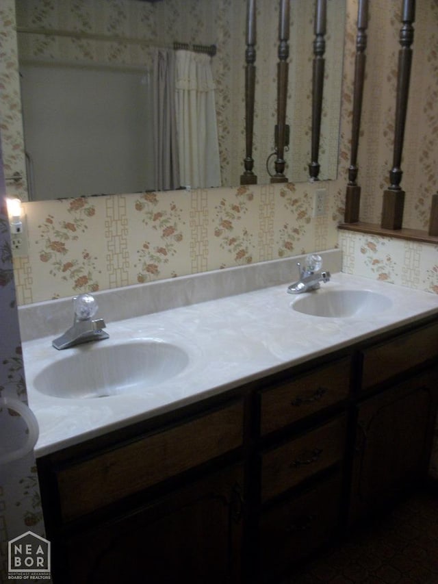 full bathroom featuring a sink, double vanity, and wallpapered walls