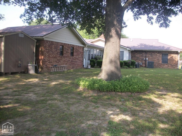 rear view of house featuring brick siding, metal roof, cooling unit, and a yard