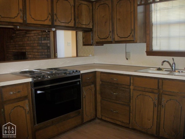 kitchen featuring range with gas cooktop, light countertops, wood finished floors, and a sink