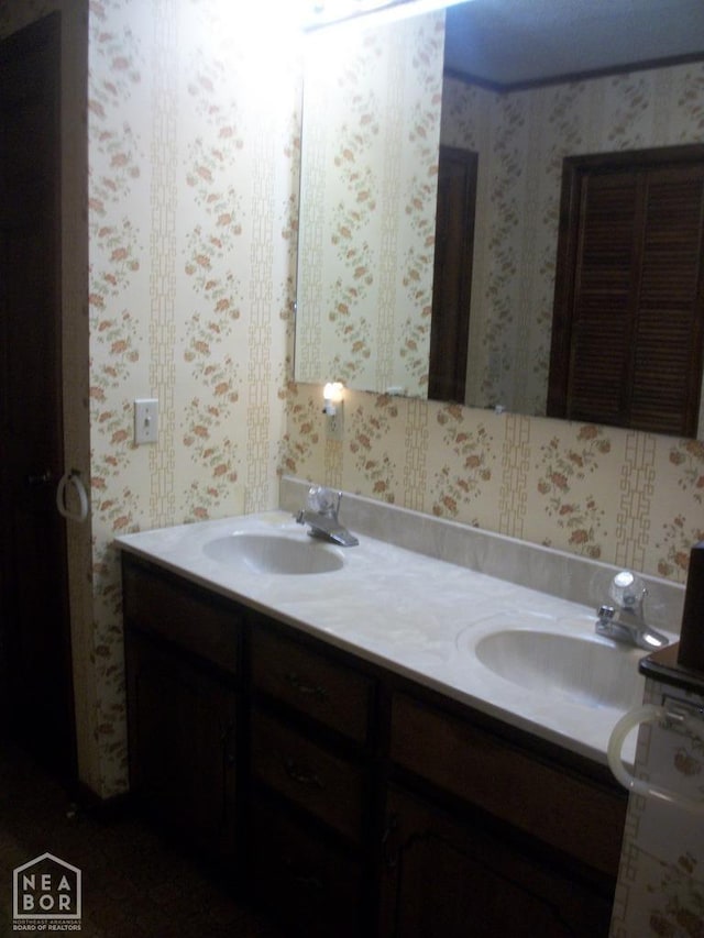 bathroom with a sink, double vanity, and wallpapered walls