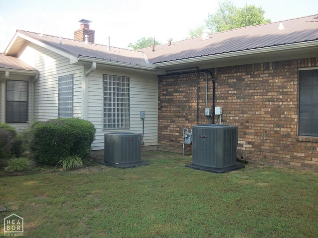 view of property exterior with a yard, brick siding, central AC, and metal roof