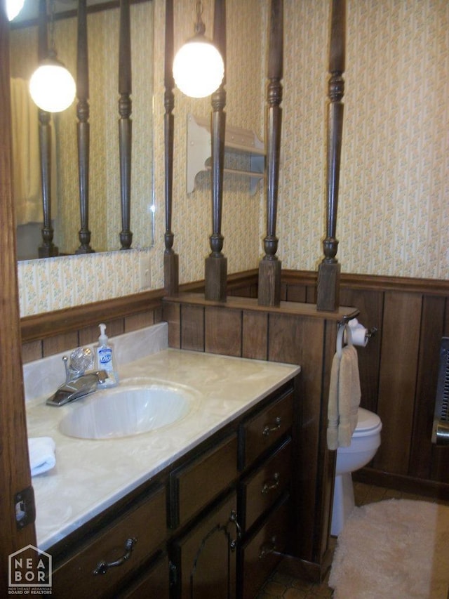 bathroom with vanity, wainscoting, wallpapered walls, and toilet