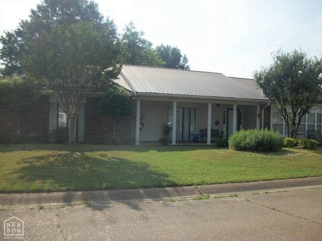 single story home featuring metal roof, a front yard, covered porch, and brick siding