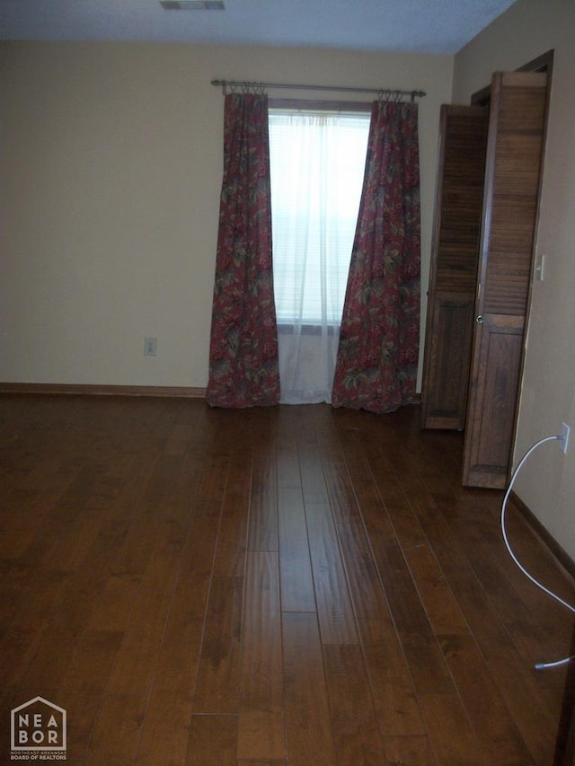 empty room with dark wood-type flooring, baseboards, and visible vents