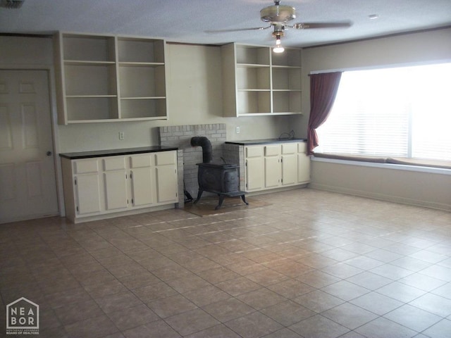 interior space featuring a wood stove, ceiling fan, baseboards, and a textured ceiling