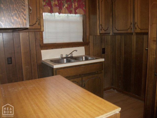 kitchen featuring light countertops, wood finished floors, wood walls, and a sink