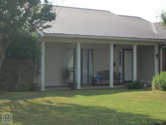 back of property featuring a yard, covered porch, metal roof, and brick siding