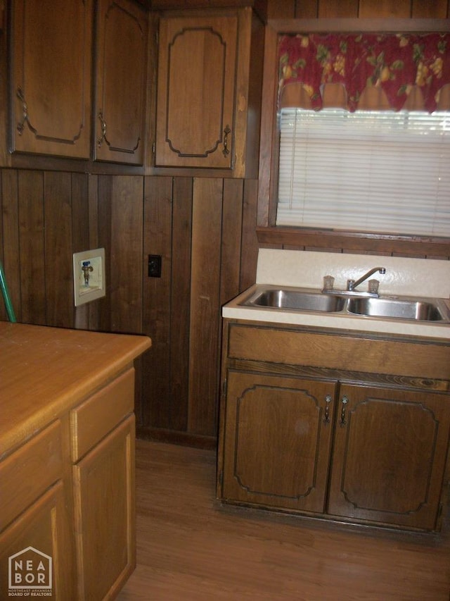 kitchen featuring light wood finished floors, light countertops, a sink, and wooden walls