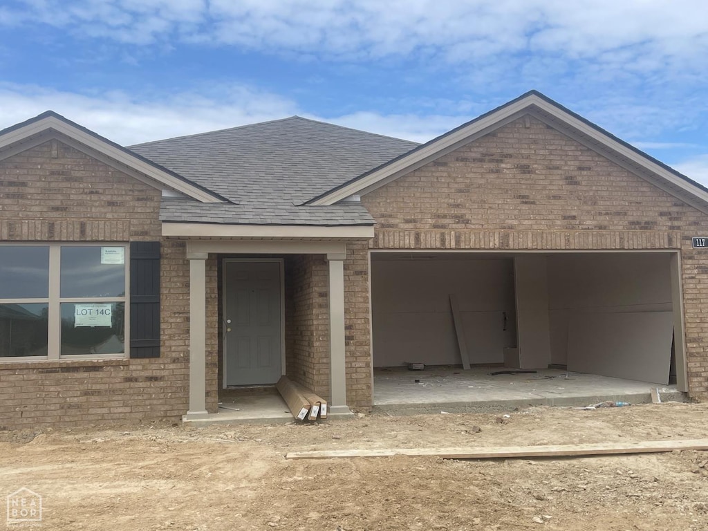 view of front of property with roof with shingles, brick siding, an attached garage, and dirt driveway