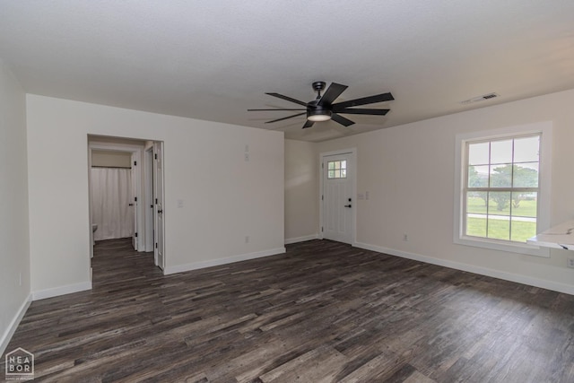 unfurnished living room with baseboards, a ceiling fan, visible vents, and dark wood-style floors