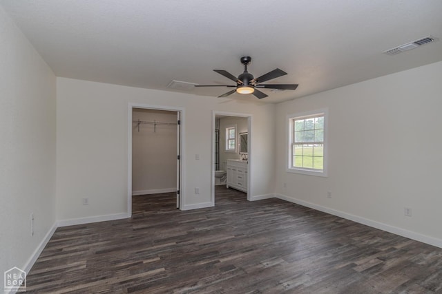 unfurnished bedroom with baseboards, visible vents, dark wood-style floors, and a walk in closet