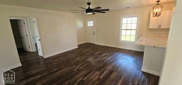 unfurnished dining area with baseboards, dark wood-style flooring, and ceiling fan with notable chandelier