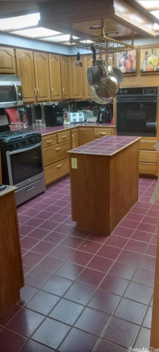 kitchen featuring dark tile patterned flooring, stainless steel appliances, ceiling fan, and a center island