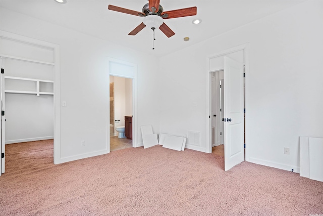 unfurnished bedroom with ensuite bathroom, ceiling fan, a closet, light colored carpet, and a walk in closet