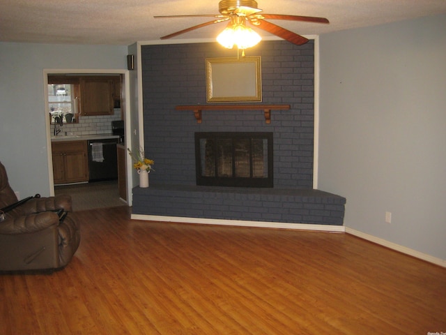 living room with wood-type flooring, a textured ceiling, a brick fireplace, and ceiling fan