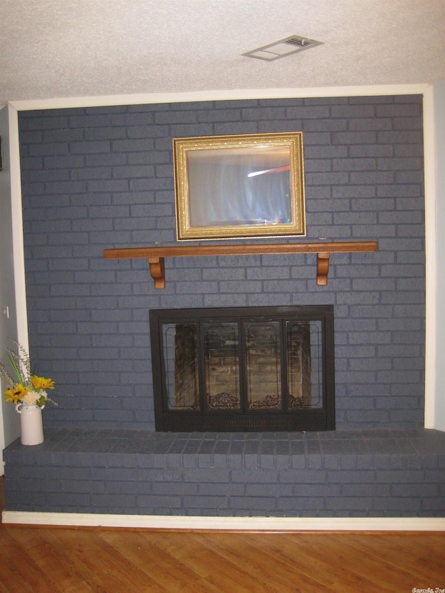 interior details featuring wood-type flooring, a textured ceiling, and a brick fireplace