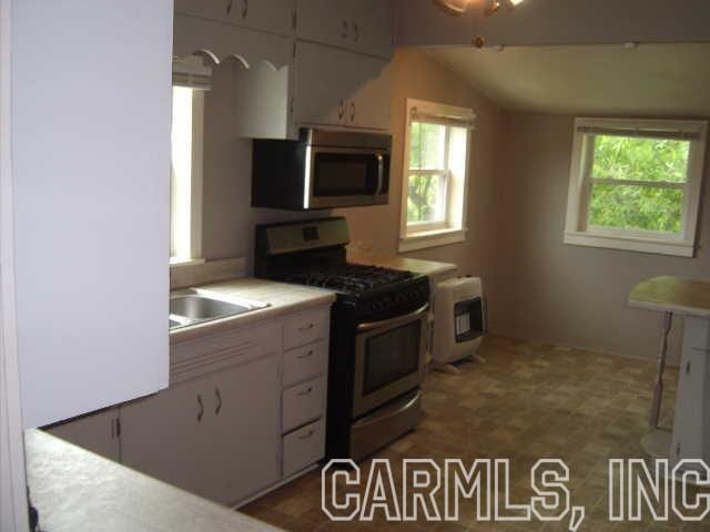 kitchen featuring white cabinets, gas range oven, dark tile flooring, and a wealth of natural light