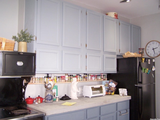 kitchen featuring white cabinets, stove, light stone countertops, and black refrigerator