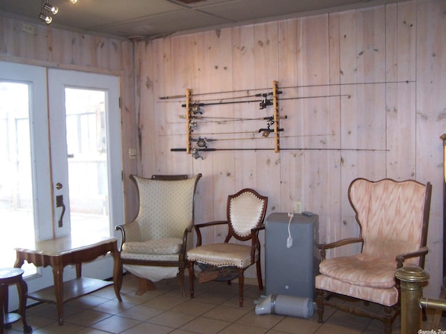 sitting room featuring french doors, light tile floors, and wooden walls