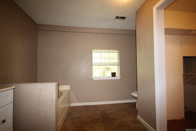 bathroom with a tub to relax in, vanity, toilet, and a textured ceiling