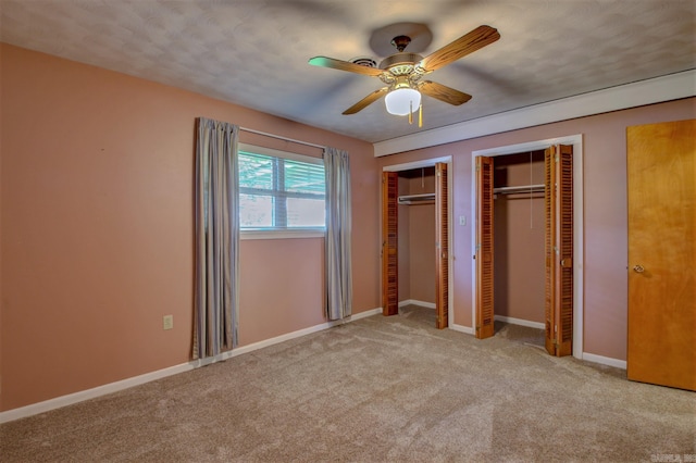 unfurnished bedroom with two closets, light colored carpet, and ceiling fan