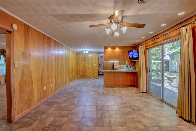 kitchen with kitchen peninsula, ceiling fan, light tile floors, wood walls, and crown molding